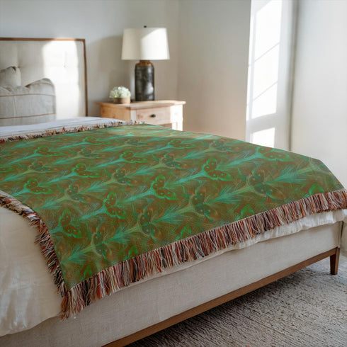 A woven cotton throw featuring an intricate luna moth design in deep green and russet tones, framed by soft fringe.